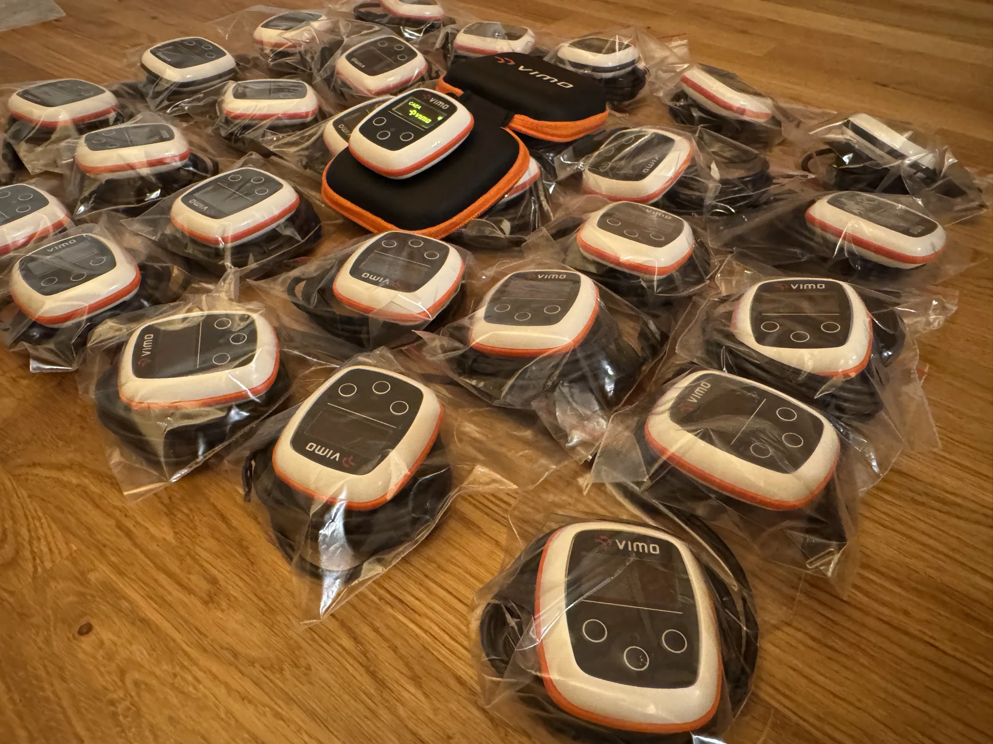 A batch of Vimo devices, each bagged with its strap, laid out on the floor