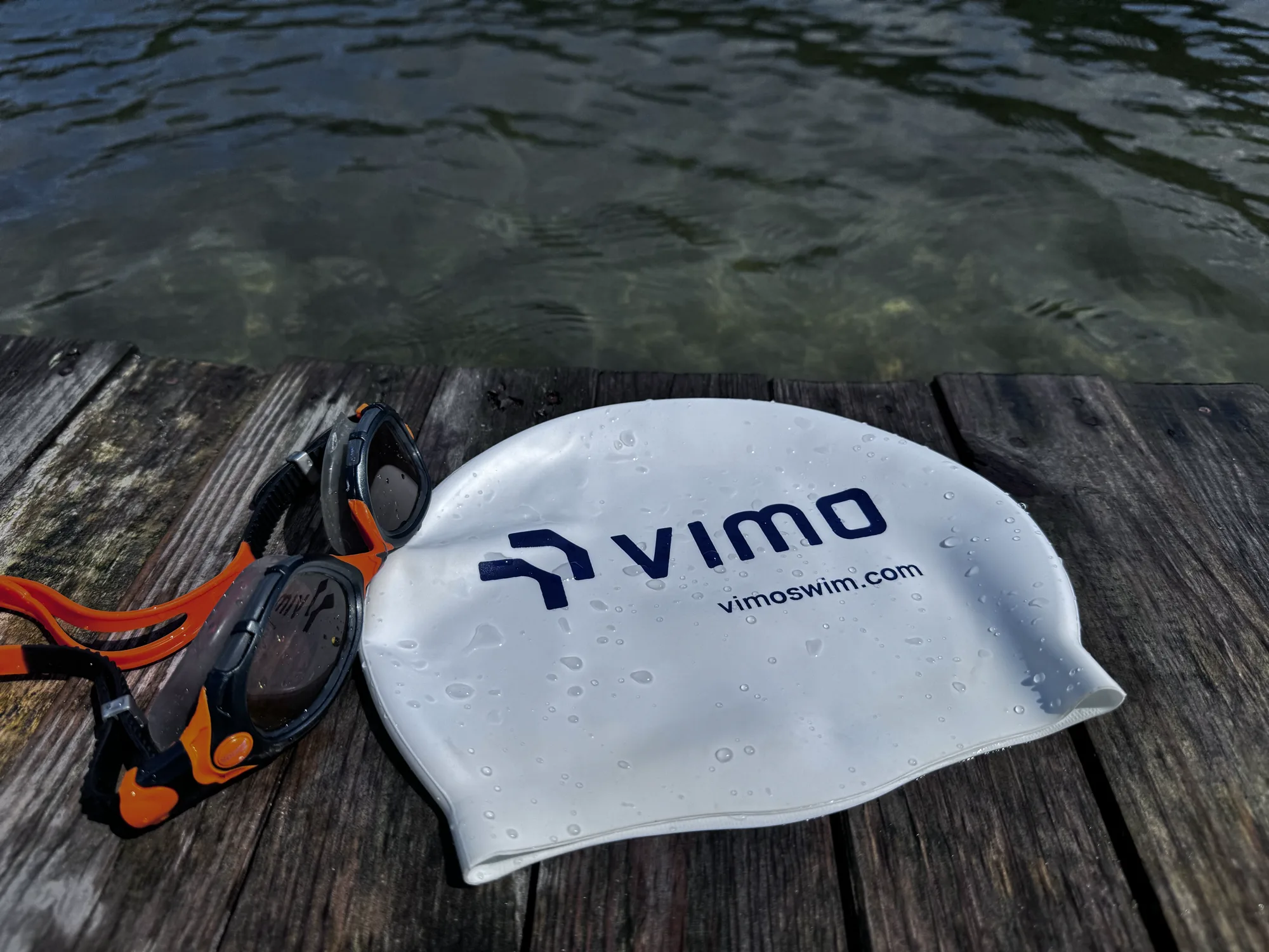 Wet Vimo swim cap and goggles on a wooden jetty